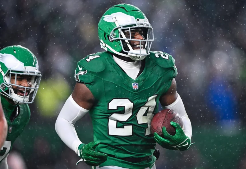 In einem grünen Trikot mit der Nummer 24 und einem Adlerlogo rennt James Bradberry mit dem Football in der Hand über das nasse Feld. Sein grüner Helm und seine weißen Handschuhe fallen im Regen auf und sorgen für eine dynamische Atmosphäre. Ein weiterer Spieler in ähnlicher Kleidung ist links teilweise zu sehen. Diese Beschreibung wurde mit der FootballR KI automatisch generiert.