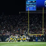 Los Angeles Chargers in Brasilien - Bei einem Footballspiel stehen Spieler in gelben und grünen Trikots in der Nähe des Torpfostens. Die Anzeigetafel zeigt einen knappen Spielstand von 18:14, 5:11 Minuten vor Ende des zweiten Viertels. Eine lebhafte Menschenmenge füllt den Hintergrund, während Banner zur Unterstützung der Los Angeles Chargers zwischen den jubelnden Fans wehen. Diese Beschreibung wurde mit der FootballR KI automatisch generiert.