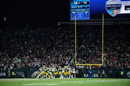 Los Angeles Chargers in Brasilien - Bei einem Footballspiel stehen Spieler in gelben und grünen Trikots in der Nähe des Torpfostens. Die Anzeigetafel zeigt einen knappen Spielstand von 18:14, 5:11 Minuten vor Ende des zweiten Viertels. Eine lebhafte Menschenmenge füllt den Hintergrund, während Banner zur Unterstützung der Los Angeles Chargers zwischen den jubelnden Fans wehen. Diese Beschreibung wurde mit der FootballR KI automatisch generiert.