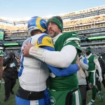 Nach einem spannenden Spiel im MetLife Stadium treffen die Giants auf NFL-Stars der gegnerischen Teams. Matthew Stafford in Blau und Gelb und Aaron Rodgers in Grün und Weiß umarmen sich herzlich, während andere Spieler und Fotografen diesen sportlichen Moment inmitten der Aufregung nach dem Spiel festhalten. Diese Beschreibung wurde mit der FootballR KI automatisch generiert.