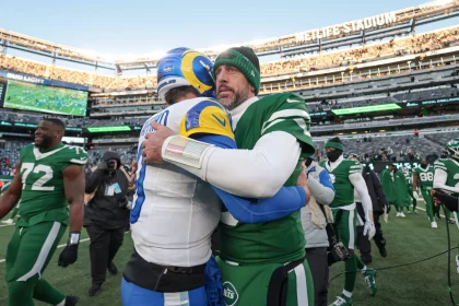 Nach einem spannenden Spiel im MetLife Stadium treffen die Giants auf NFL-Stars der gegnerischen Teams. Matthew Stafford in Blau und Gelb und Aaron Rodgers in Grün und Weiß umarmen sich herzlich, während andere Spieler und Fotografen diesen sportlichen Moment inmitten der Aufregung nach dem Spiel festhalten. Diese Beschreibung wurde mit der FootballR KI automatisch generiert.