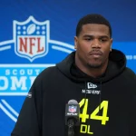 Abdul Carter in einem schwarzen Kapuzenpullover mit der Aufschrift „44“ steht ernst vor einem Mikrofon mit dem NFL-Logo. Der blaue Hintergrund mit dem Scouting Combine-Branding deutet auf seine Entschlossenheit hin. Abdul Carters intensive Konzentration lässt darauf schließen, dass er für den nächsten großen Schritt in seiner Karriere bereit ist. Diese Beschreibung wurde mit der FootballR KI automatisch generiert.