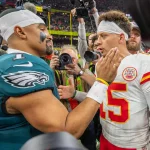 Woche 2 Free TV - Zwei American-Football-Spieler interagieren während des Super Bowl LIX auf dem Spielfeld, umgeben von Fotografen. Der Spieler links trägt ein blaugrünes Eagles-Trikot, während der Spieler rechts ein weißes Chiefs-Trikot trägt. Kameras und Fans stehen im Hintergrund und halten diesen ikonischen Moment fest. Diese Beschreibung wurde mit der FootballR KI automatisch generiert.