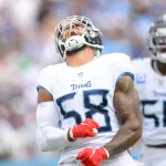 Harold Landry in der Uniform der Titans, Nummer 58, feiert triumphierend auf dem Feld, den Kopf in den Nacken gelegt und die Arme gestreckt. Daneben steht Nummer 55. Mit sichtbaren Tattoos und Handschuhen schwelgt Harold Landry vor dem Hintergrund verschwommener jubelnder Fans in seinem Sieg. Diese Beschreibung wurde mit der FootballR KI automatisch generiert.