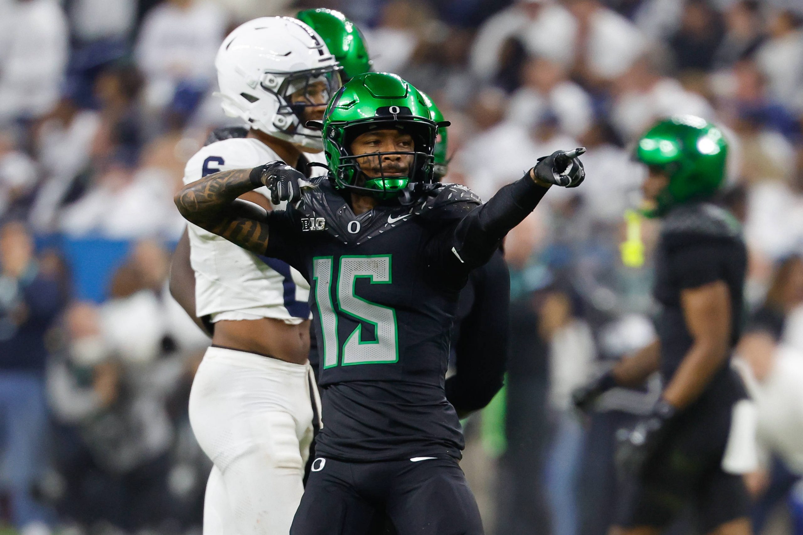 Ein Footballspieler, möglicherweise Tez Johnson, in schwarzer Uniform mit grünen Akzenten, zeigt mit beiden Händen. Sein glänzend grüner Helm glänzt im Stadionlicht. Ein weiterer Spieler in Weiß verweilt im Hintergrund, während die Fans die Tribünen füllen und die Spannung des Spiels auf dem Spielfeld einfangen. Diese Beschreibung wurde mit der FootballR KI automatisch generiert.