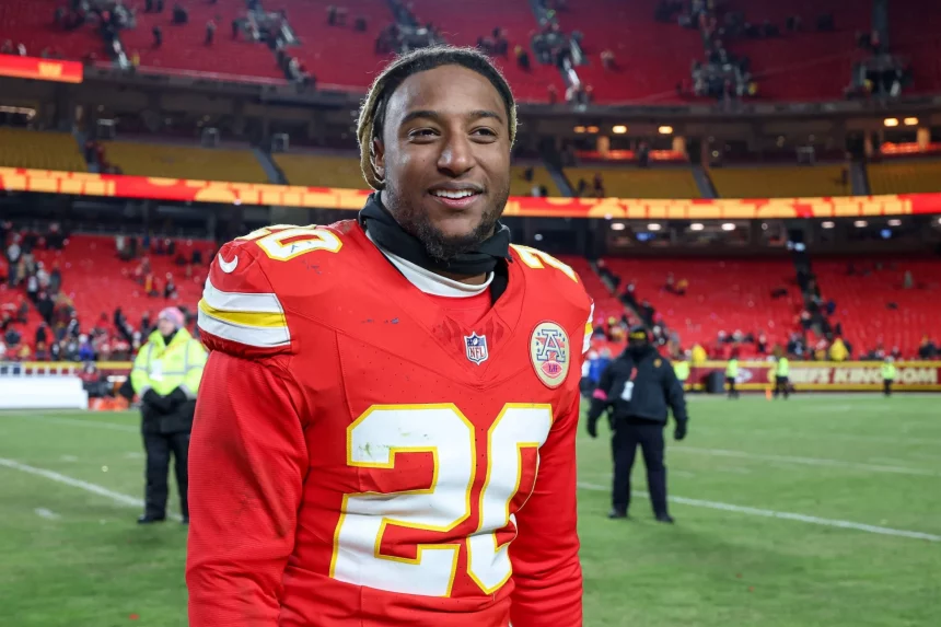 Justin Reid in der roten Uniform der Kansas City Chiefs, Nummer 20, lächelt auf dem Spielfeld. Das Stadion ist fast leer, im Hintergrund stehen ein paar Leute. Justin Reid hat kurze Haare und trägt einen schwarzen Halswärmer. Die Atmosphäre lässt vermuten, dass ein Spiel gerade zu Ende gegangen ist. Diese Beschreibung wurde mit der FootballR KI automatisch generiert.