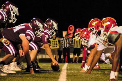 Unter den hellen Stadionlichtern eines klassischen College-Football-Duells stehen sich zwei amerikanische Teams an der Line of Scrimmage gegenüber. Die kastanienbraun gekleideten Spieler treten gegen ihre Rivalen in Rot und Gelb an. Schiedsrichter und eine Yard-Markierung wachen auf dem sattgrünen Rasen und präsentieren die aufstrebenden Talente der USA. Diese Beschreibung wurde mit der FootballR KI automatisch generiert.