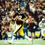 Ein Quarterback von Pittsburgh in schwarz-gelber Uniform bereitet sich während des Spiels auf einen Pass vor. Mit einem schwarzen Helm mit dem Teamlogo steht er inmitten jubelnder Zuschauer. Der Schiedsrichter beobachtet gespannt, wie sich auf dem leuchtend grünen Spielfeld der entscheidende Moment nähert. Diese Beschreibung wurde mit der FootballR KI automatisch generiert.