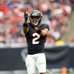 Ein Footballspieler, Robert Woods, steht in einem schwarzen Trikot mit der Nummer 2 und weißen Hosen auf dem Spielfeld. Er zeigt mit der rechten Hand nach oben und gestikuliert mit der linken. Er trägt Helm und Handschuhe. Im Hintergrund ist ein unscharfes Stadionpublikum zu sehen. Diese Beschreibung wurde mit der FootballR KI automatisch generiert.