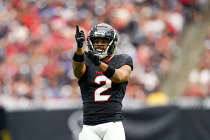 Ein Footballspieler, Robert Woods, steht in einem schwarzen Trikot mit der Nummer 2 und weißen Hosen auf dem Spielfeld. Er zeigt mit der rechten Hand nach oben und gestikuliert mit der linken. Er trägt Helm und Handschuhe. Im Hintergrund ist ein unscharfes Stadionpublikum zu sehen. Diese Beschreibung wurde mit der FootballR KI automatisch generiert.