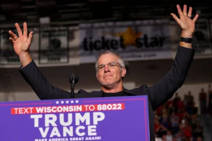 Brett Favre reckt triumphierend die Arme hinter einem Podium bei der politischen Kundgebung „Trump Vance 2024“. Im Hintergrund sind eine verschwommene Menschenmenge, ein „Ticket Star“-Banner und Gerüchte über Brett Favres Einfluss zu sehen, während die Szene vor Energie über das Texten von Wisconsin sprüht. Diese Beschreibung wurde mit der FootballR KI automatisch generiert.