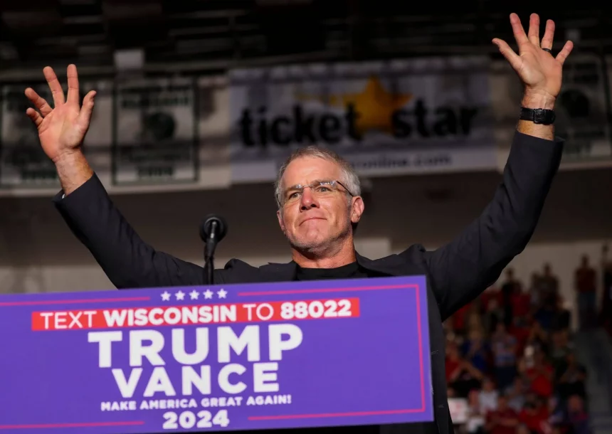 Brett Favre reckt triumphierend die Arme hinter einem Podium bei der politischen Kundgebung „Trump Vance 2024“. Im Hintergrund sind eine verschwommene Menschenmenge, ein „Ticket Star“-Banner und Gerüchte über Brett Favres Einfluss zu sehen, während die Szene vor Energie über das Texten von Wisconsin sprüht. Diese Beschreibung wurde mit der FootballR KI automatisch generiert.