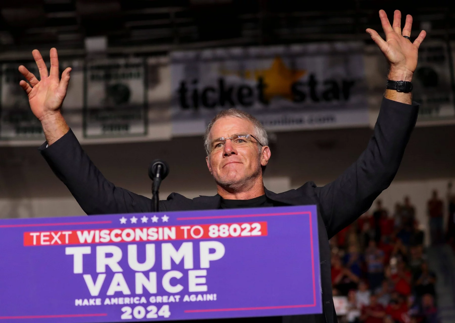 Brett Favre reckt triumphierend die Arme hinter einem Podium bei der politischen Kundgebung „Trump Vance 2024“. Im Hintergrund sind eine verschwommene Menschenmenge, ein „Ticket Star“-Banner und Gerüchte über Brett Favres Einfluss zu sehen, während die Szene vor Energie über das Texten von Wisconsin sprüht. Diese Beschreibung wurde mit der FootballR KI automatisch generiert.