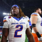 Boise State Runningback Ashton Jeanty, Trikotnummer 2, mit Dreadlocks und blauem Stirnband, steht nach einem Spiel auf dem Spielfeld. Seine fleckige Uniform lässt auf seinen Biss schließen – vielleicht ein Vorbote für die NFL Draft 2025. Diese Beschreibung wurde mit der FootballR KI automatisch generiert.