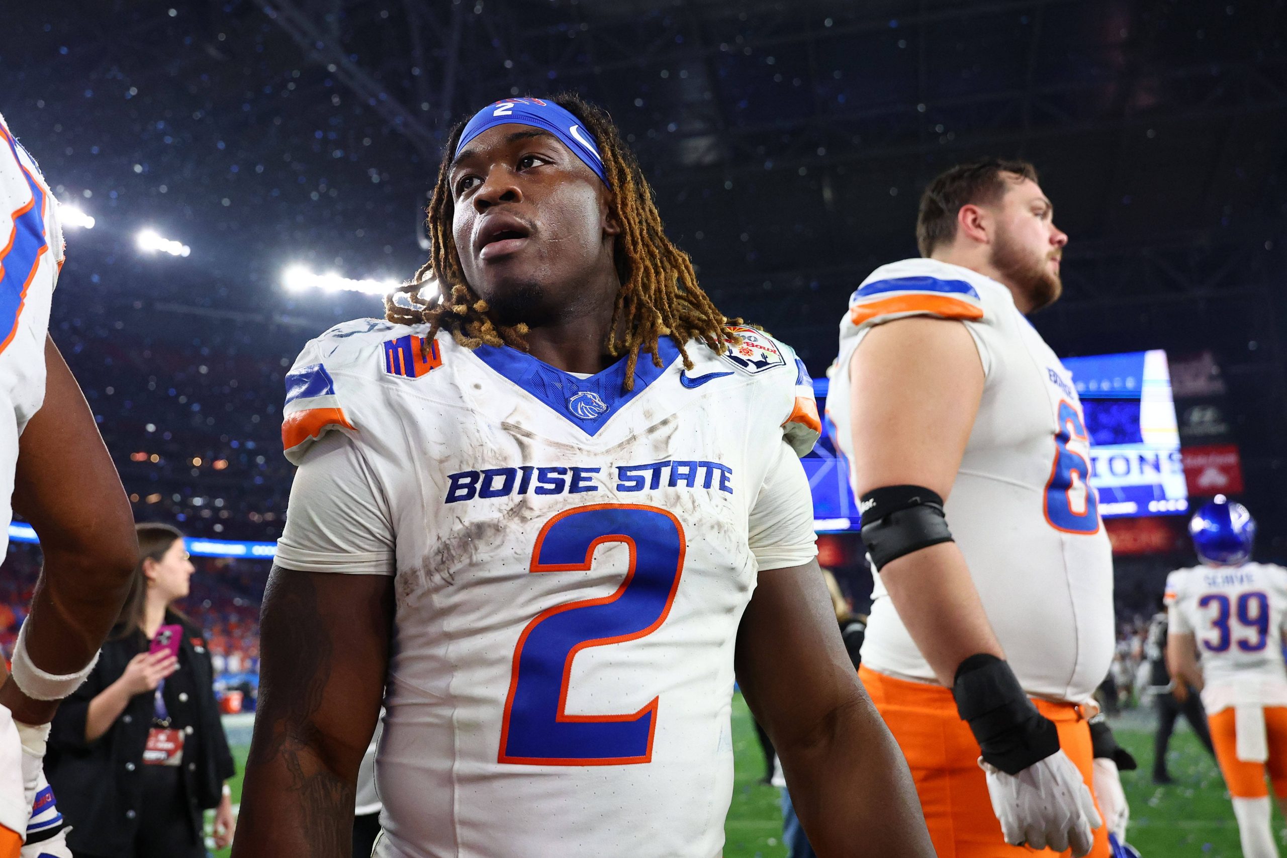 Boise State Runningback Ashton Jeanty, Trikotnummer 2, mit Dreadlocks und blauem Stirnband, steht nach einem Spiel auf dem Spielfeld. Seine fleckige Uniform lässt auf seinen Biss schließen – vielleicht ein Vorbote für die NFL Draft 2025. Diese Beschreibung wurde mit der FootballR KI automatisch generiert.