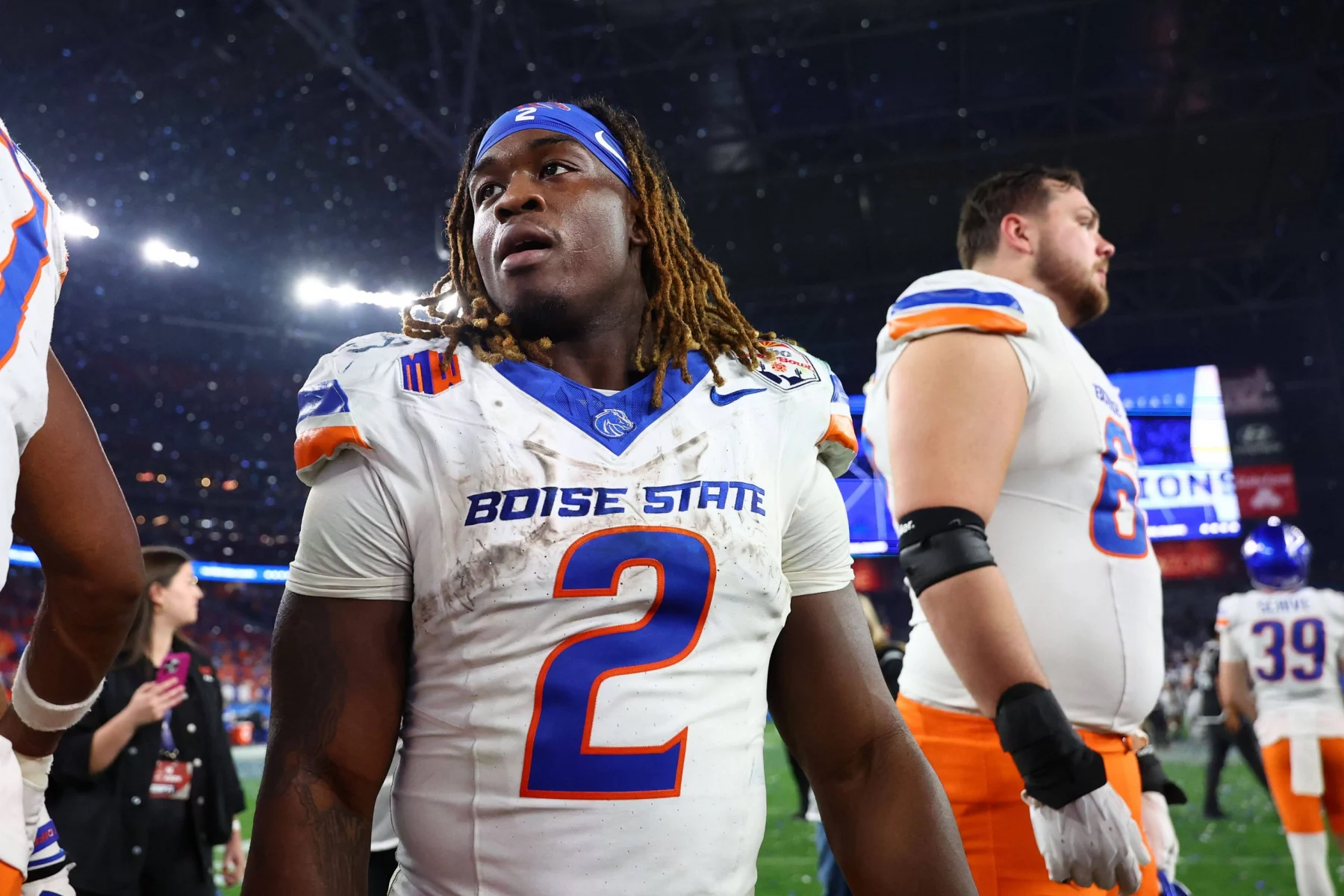 Boise State Runningback Ashton Jeanty, Trikotnummer 2, mit Dreadlocks und blauem Stirnband, steht nach einem Spiel auf dem Spielfeld. Seine fleckige Uniform lässt auf seinen Biss schließen – vielleicht ein Vorbote für die NFL Draft 2025. Diese Beschreibung wurde mit der FootballR KI automatisch generiert.
