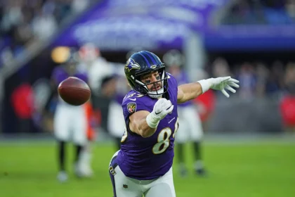 Mark Andrews, Footballspieler im lila Trikot der Baltimore Ravens, streckt beide Hände aus, als ein Football an ihm vorbeifliegt. Das Spielfeld und die gegnerischen Spieler sind im Hintergrund verschwommen, was den Fokus und die Dynamik des Spiels unterstreicht. Diese Beschreibung wurde mit der FootballR KI automatisch generiert.