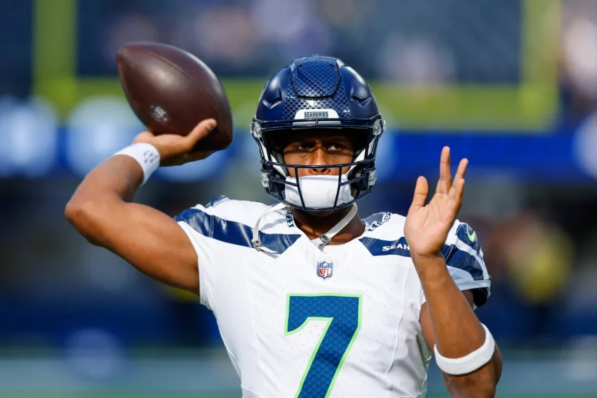 Geno Smith in einem weiß-blauen Trikot mit der Nummer 7, das an einen Klassiker aus Darnold vs. Smith erinnert, bereitet sich auf einen Footballwurf vor. Mit blauem Helm und Visier steht er hochkonzentriert vor dem Hintergrund eines verschwommenen Stadions, in dem das Spielgeschehen pulsiert. Diese Beschreibung wurde mit der FootballR KI automatisch generiert.
