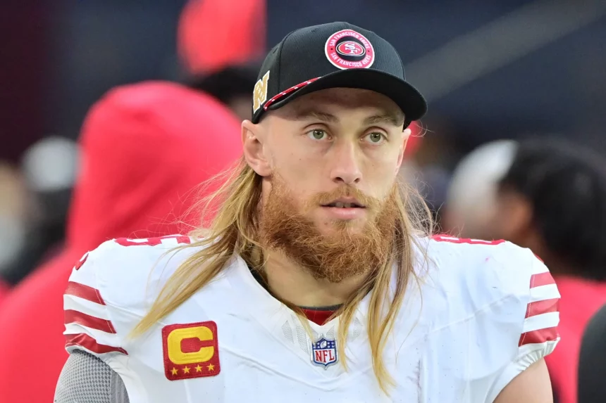 Fantasy Football Woche 7 - Ein Footballspieler mit langen blonden Haaren und rötlichem Bart trägt die Uniform der San Francisco 49ers und eine schwarze Kappe. Auf seinem weißen Trikot trägt er – wie Star-Tight-End George Kittle – einen Kapitänsaufnäher und blickt mit neutralem Gesichtsausdruck nach vorn. Diese Beschreibung wurde mit der FootballR KI automatisch generiert.