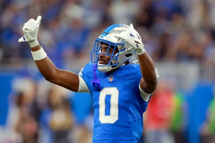 Detroit-Lion-Spieler Terrion Arnold in blauer Uniform und silbernem Helm streckt während eines Spiels beide Arme mit gebeugten Händen in die Höhe. Mit der Nummer 0 sticht er aus der verschwommenen Menge hervor und fängt die aufregende Stadionatmosphäre ein. Diese Beschreibung wurde mit der FootballR KI automatisch generiert.