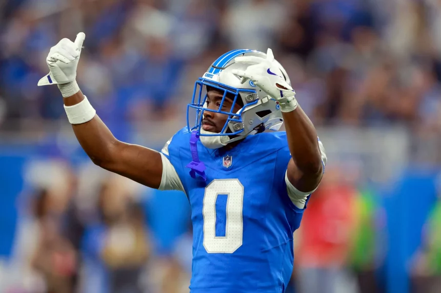 Detroit-Lion-Spieler Terrion Arnold in blauer Uniform und silbernem Helm streckt während eines Spiels beide Arme mit gebeugten Händen in die Höhe. Mit der Nummer 0 sticht er aus der verschwommenen Menge hervor und fängt die aufregende Stadionatmosphäre ein. Diese Beschreibung wurde mit der FootballR KI automatisch generiert.