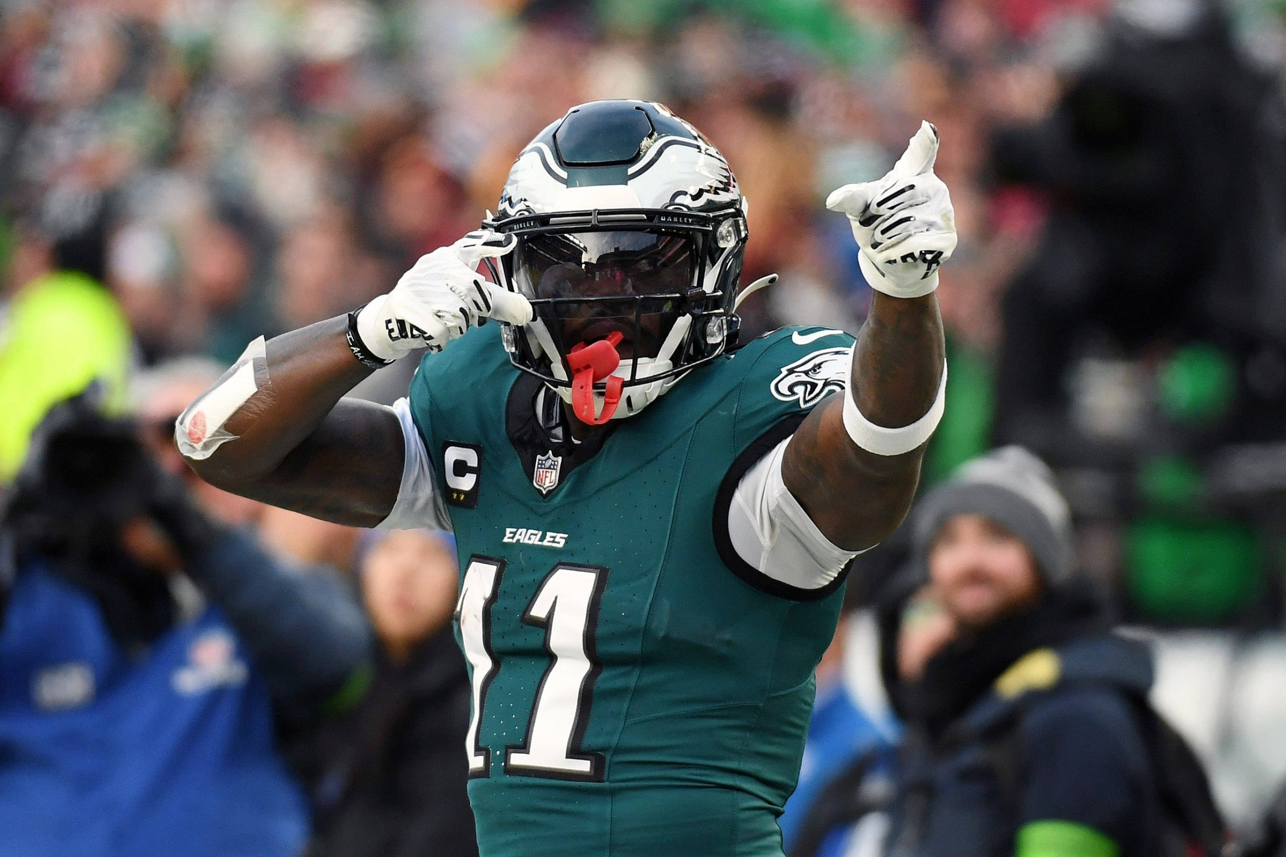 NFL Power Ranking - A.J. Brown in der grünen Philadelphia-Eagles-Uniform mit der Nummer 11 und schwarzem Helm zeigt während eines Spiels mit beiden Händen auf seinen Helm, als wolle er um Aufmerksamkeit bitten, wie jemand, der nach einem gestohlenen Auto sucht. Im Hintergrund sind verschwommene Zuschauer zu sehen. Diese Beschreibung wurde mit der FootballR KI automatisch generiert.