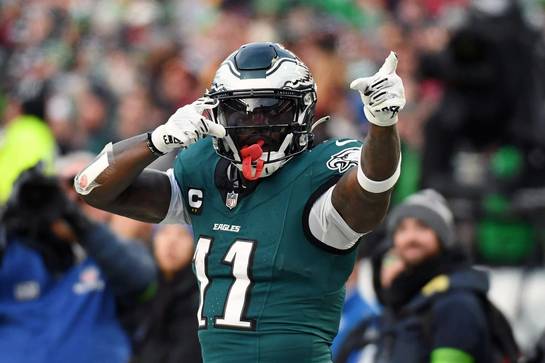Free Agency - NFL Power Ranking - A.J. Brown in der grünen Philadelphia-Eagles-Uniform mit der Nummer 11 und schwarzem Helm zeigt während eines Spiels mit beiden Händen auf seinen Helm, als wolle er um Aufmerksamkeit bitten, wie jemand, der nach einem gestohlenen Auto sucht. Im Hintergrund sind verschwommene Zuschauer zu sehen. Diese Beschreibung wurde mit der FootballR KI automatisch generiert.