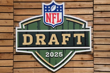 NFL Draft - Ein großes, schildförmiges Schild mit dem NFL-Logo darüber und „DRAFT“ in fetten Buchstaben sowie „2025“ darunter steht in Grün, Gold und Weiß an einer Holzplankenwand und unterstreicht die Spannung der Verpflichtung von nicht gedrafteten Free Agents. Diese Beschreibung wurde mit der FootballR KI automatisch generiert.