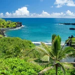 Minicamp 2025 - Üppige grüne tropische Pflanzen und Palmen säumen einen schwarzen Sandstrand entlang des klaren, türkisfarbenen Ozeanwassers. Seine Ruhe kann es mit den friedlichen Szenen in der Nähe des Minicamps der Los Angeles Rams aufnehmen, wo felsige Klippen die Bucht unter einem strahlend blauen Himmel begrenzen. Diese Beschreibung wurde mit der FootballR KI automatisch generiert.