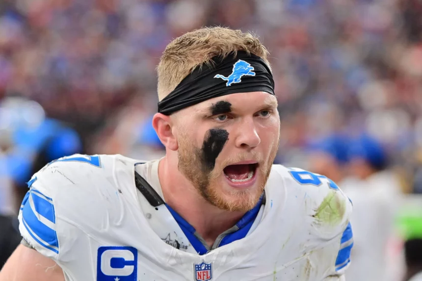 Aidan Hutchinson, ein Footballspieler der Detroit Lions mit schwarzem Stirnband, schwarzer Augenfarbe und schmutzig-weißer Uniform, schreit während eines Spiels lautstark. Der Stadionhintergrund ist unscharf, was seinen emotionalen und kämpferischen Ausdruck unterstreicht. Diese Beschreibung wurde mit der FootballR KI automatisch generiert.