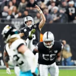 AJ Cole, mit der Nummer 6 in einem schwarzen Trikot der Las Vegas Raiders, kickt den Ball während eines Spiels. Teamkollegen und Gegner in Jaguars-Trikots sind auf dem Feld. Die Zuschauer sind im Hintergrund verschwommen und fangen die Dynamik und Intensität des Spiels ein. Diese Beschreibung wurde mit der FootballR KI automatisch generiert.