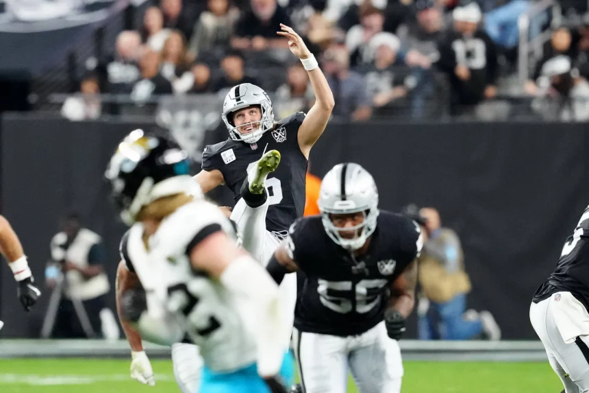 AJ Cole, mit der Nummer 6 in einem schwarzen Trikot der Las Vegas Raiders, kickt den Ball während eines Spiels. Teamkollegen und Gegner in Jaguars-Trikots sind auf dem Feld. Die Zuschauer sind im Hintergrund verschwommen und fangen die Dynamik und Intensität des Spiels ein. Diese Beschreibung wurde mit der FootballR KI automatisch generiert.