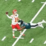 Route Concepts - Ein Footballspieler in der roten Uniform der Kansas City Chiefs (#15) bereitet sich darauf vor, den Ball zu werfen und demonstriert dabei scharfe Routenkonzepte, während er von einem grünen Spieler der Philadelphia Eagles (#94) auf einem grünen Feld mit weißen Yard-Linien getackelt wird. Diese Beschreibung wurde mit der FootballR KI automatisch generiert.