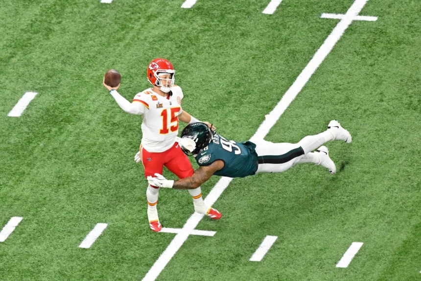 Heute im TV - Route Concepts - Ein Footballspieler in der roten Uniform der Kansas City Chiefs (#15) bereitet sich darauf vor, den Ball zu werfen und demonstriert dabei scharfe Routenkonzepte, während er von einem grünen Spieler der Philadelphia Eagles (#94) auf einem grünen Feld mit weißen Yard-Linien getackelt wird. Diese Beschreibung wurde mit der FootballR KI automatisch generiert.
