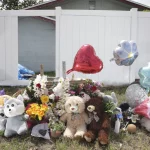 Miami Hurricanes Spieler in Unfall verwickelt: Ein Denkmal mit Teddybären, Stofftieren, Blumen und herz- und blumenförmigen Luftballons steht auf dem Rasen vor einem weißen Zaun und einem Haus – einige Gegenstände ehren die Verstorbenen mit herzlichen Botschaften der Erinnerung und des Beileids. Diese Beschreibung wurde mit der FootballR KI automatisch generiert.