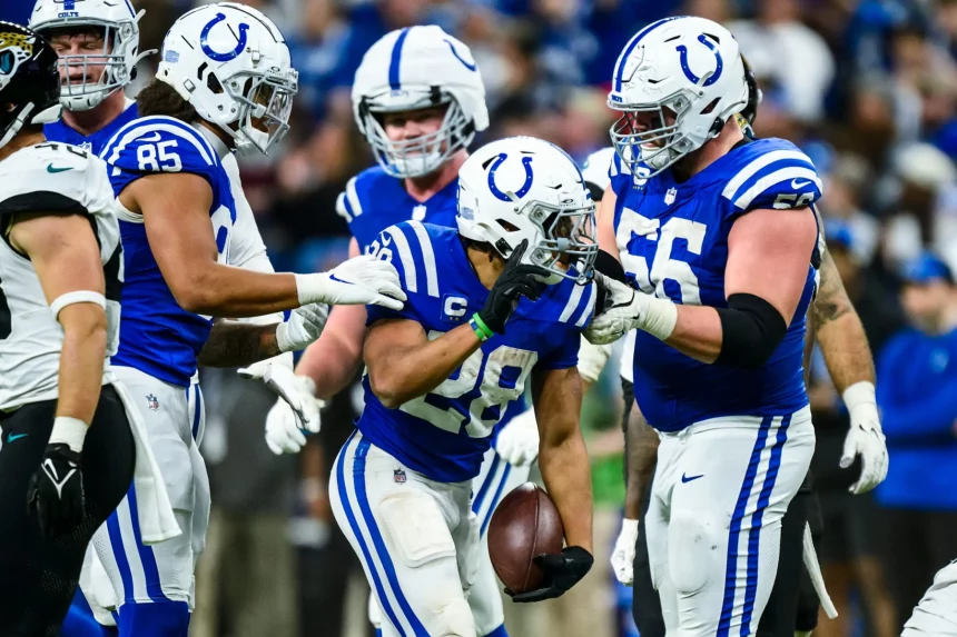 Footballspieler der Indianapolis Colts in blau-weißen Trikots feiern auf dem Spielfeld. Ein Spieler der Indianapolis Colts hält den Ball und ist während des Spiels von Teamkollegen umringt, die ihm gratulieren. Im unscharfen Hintergrund ist eine jubelnde Menge zu sehen. Diese Beschreibung wurde mit der FootballR KI automatisch generiert.