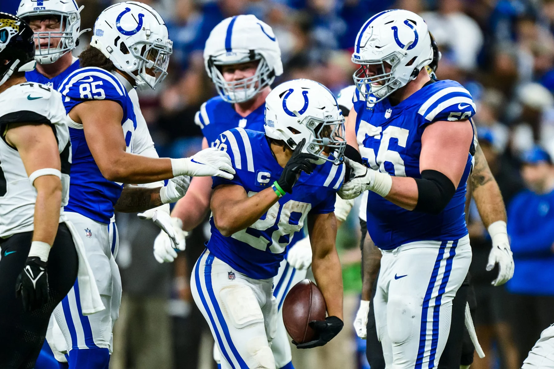 Footballspieler der Indianapolis Colts in blau-weißen Trikots feiern auf dem Spielfeld. Ein Spieler der Indianapolis Colts hält den Ball und ist während des Spiels von Teamkollegen umringt, die ihm gratulieren. Im unscharfen Hintergrund ist eine jubelnde Menge zu sehen. Diese Beschreibung wurde mit der FootballR KI automatisch generiert.