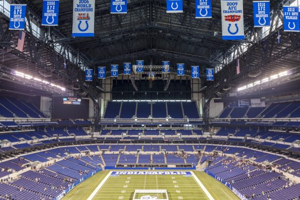 Woche 11 - Ein weiter Blick auf ein leeres Footballstadion mit blauen Sitzen und Bannern, darunter Colts-Logos und Meisterschaftsjahre. In der Endzone steht „INDIANAPOLIS“ – ein Hinweis darauf, dass es die Heimat der Indianapolis Colts ist und das Erbe der Irsay Schwestern ehrt. Diese Beschreibung wurde mit der FootballR KI automatisch generiert.