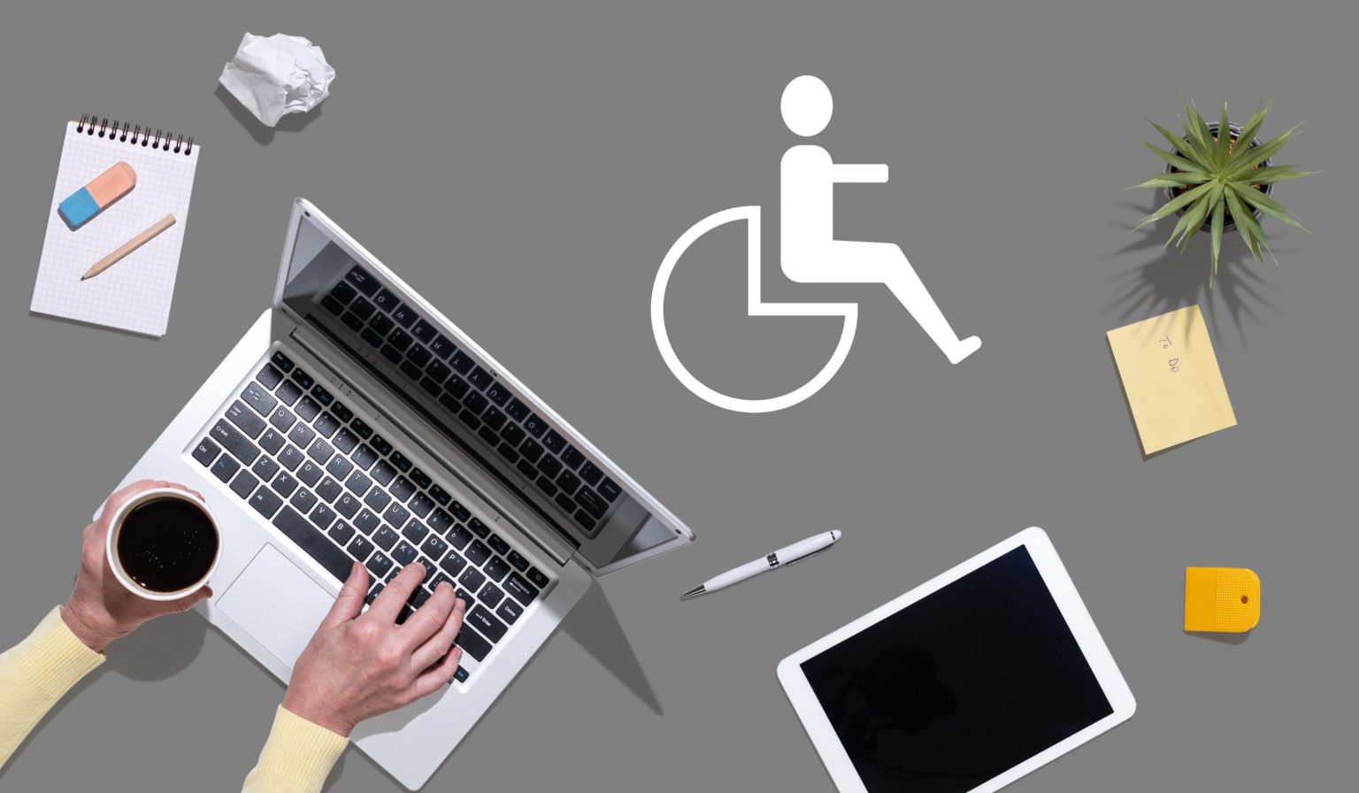 Die linke Hand einer Person benutzt einen Laptop neben einer Tasse Kaffee, einem Notizblock, einem Stift, einem Radiergummi, zerknittertem Papier, Haftnotizen, einer Pflanze und einer Tafel auf einer grauen Oberfläche. Ein weißes Symbol für Barrierefreiheit in der Mitte symbolisiert die Barrierefreiheitserklärung. Diese Beschreibung wurde mit der FootballR KI automatisch generiert.