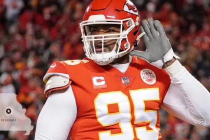 Chiefs und Royals - Ein Footballspieler im roten Trikot der Kansas City Chiefs (Nummer 95) hebt seine linke Hand ans Ohr, als würde er zuhören. Die verschwommene Stadionmenge deutet auf große Stadionprojekte hin. In der Ecke ist die Umrisslinie des Staates Missouri mit einem Stern und dem Schriftzug „MISSOURI“ zu sehen. Diese Beschreibung wurde mit der FootballR KI automatisch generiert.