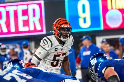Germaine Pratt, ein Footballspieler der Cincinnati Bengals in weißer Uniform und orange gestreiftem Helm, steht der Offensive Line der New York Giants in blauen Uniformen gegenüber und bereitet sich auf einen Spielzug vor. Im Hintergrund sind Trainer, eine digitale Anzeigetafel und Stadionlichter zu sehen. Diese Beschreibung wurde mit der FootballR KI automatisch generiert.