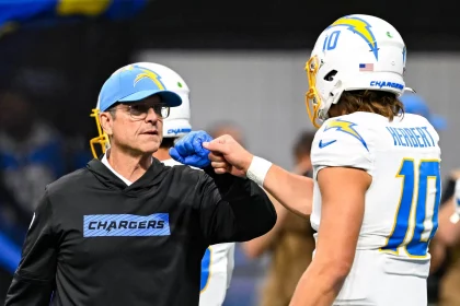 Ein Chargers-Trainer in einem schwarzen Kapuzenpulli und einer blauen Mütze stößt Justin Herbert, der eine weiße Chargers-Uniform und einen Helm mit der Nummer 10 trägt, mit der Faust an. Der unscharfe Hintergrund lenkt den Fokus auf ihre Jubelgeste. Diese Beschreibung wurde mit der FootballR KI automatisch generiert.