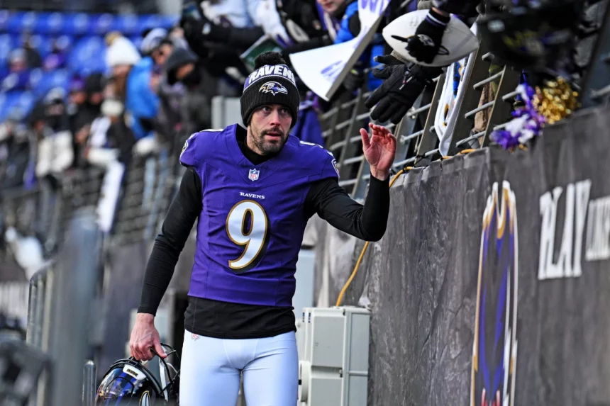 Der NFL-Spieler Justin Tucker von den Baltimore Ravens, der ein lila Trikot mit der Nummer 9 und eine Mütze trägt, gibt den Fans über das Stadiongeländer ein High Five. Er hält seinen Helm in einer Hand und blickt nach oben, während die Menge Fahnen schwenkt und sich begeistert die Hände reicht. Diese Beschreibung wurde mit der FootballR KI automatisch generiert.