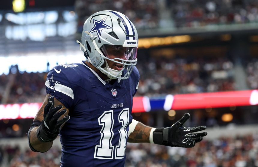 Dallas Cowboys-Star Micah Parsons, Trikotnummer 11, silberner Helm und schwarze Handschuhe, steht mit erhobenen Händen und ausdrucksstarkem Gesicht auf dem Spielfeld. Im Hintergrund leuchten die Zuschauer und die Stadionlichter unscharf. Diese Beschreibung wurde mit der FootballR KI automatisch generiert.