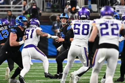 Pressure Packages und Bltiz-Design - Ein Football-Quarterback in einem schwarzen Trikot (Carolina Panthers) versucht während eines Spiels einen Pass zu spielen, während er von drei Verteidigern in weißen Trikots (Minnesota Vikings) verfolgt wird, während andere Spieler blocken und die Menge im Hintergrund verschwommen ist. Diese Beschreibung wurde mit der FootballR KI automatisch generiert.