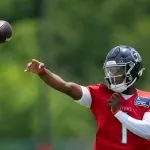 Ein Footballspieler namens Cam Ward, in einem roten Trainingstrikot und einem dunklen Helm mit der Aufschrift „TITANS“, wirft mit der rechten Hand einen Football. Er trägt einen weißen Ärmel und steht im Freien vor verschwommenen grünen Bäumen. Diese Beschreibung wurde mit der FootballR KI automatisch generiert.