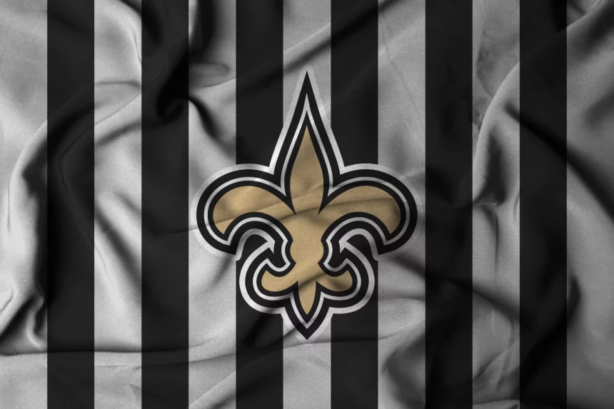 Paris - New Orleans Saints - Ein zerknitterter Stoff mit abwechselnd schwarzen und grauen vertikalen Streifen. In der Mitte befindet sich eine große goldene Fleur-de-Lis, das ikonische Logo der New Orleans Saints. Die Falten des Stoffes erzeugen Schatten und Textur, die das Design der neuen Farbe noch besser zur Geltung bringen. Diese Beschreibung wurde mit der FootballR KI automatisch generiert.