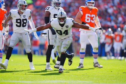 Ein Football-Spieler, Christian Wilkins, in einem weißen Las Vegas Raiders-Trikot (#94) breitet seine Arme zum Jubel auf dem Spielfeld aus, umgeben von Mannschaftskameraden und Denver Broncos-Spielern in orangefarbenen Uniformen; Sonnenlicht beleuchtet die Aktion. Diese Beschreibung wurde mit der FootballR KI automatisch generiert.