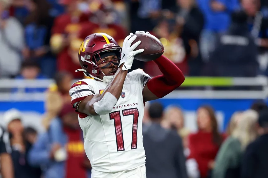 Terry McLaurin, der ein weißes Trikot der Washington Commanders mit der Nummer 17 trägt, fängt während eines Spiels einen Football, während Zuschauer und andere Spieler im Hintergrund verschwimmen. Diese Beschreibung wurde mit der FootballR KI automatisch generiert.