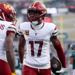 Zwei Footballspieler der Washington Commanders feiern auf dem Spielfeld. Terry McLaurin, Nummer 17, hält einen Ball und ruft der Nummer 14 energisch zu. Beide tragen weiße Trikots mit burgunderroten und goldenen Akzenten, während Spieler der Philadelphia Eagles unscharf zu sehen sind. Diese Beschreibung wurde mit der FootballR KI automatisch generiert.